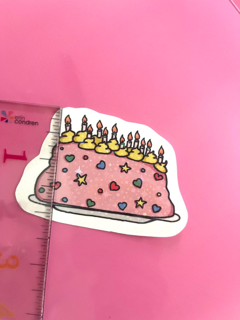 Peut inclure: Un g&acirc;teau rose avec un gla&ccedil;age jaune et des bougies. Le g&acirc;teau est d&eacute;cor&eacute; de vermicelles color&eacute;s, d'&eacute;toiles et de c&oelig;urs.