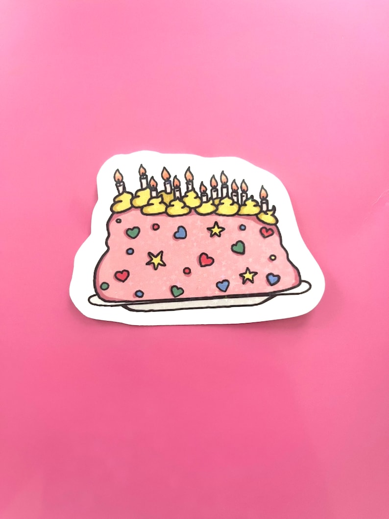 Peut inclure: Un g&acirc;teau d'anniversaire rose avec un gla&ccedil;age jaune et des bougies. Le g&acirc;teau est d&eacute;cor&eacute; de vermicelles color&eacute;s, y compris des c&oelig;urs et des &eacute;toiles.