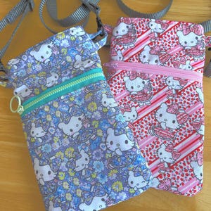 May include: Two small crossbody bags with adjustable gray straps. One bag is patterned with Hello Kitty characters and flowers on a blue background, and the other has a pink and red Hello Kitty design. Both have zippered closures.