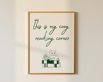 Könnte beinhalten: Ein gerahmter Druck mit goldenem Rahmen zeigt den Text "This is my cozy reading corner" in grüner Schrift. Darunter eine grüne Strichzeichnung einer Katze auf einem Stapel Bücher. Der Hintergrund ist cremeweiß.