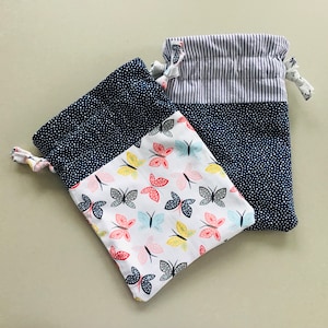 May include: Two drawstring bags. One bag features a navy blue polka dot pattern with a white butterfly print. The other bag has a navy blue polka dot pattern with a white and blue striped top.