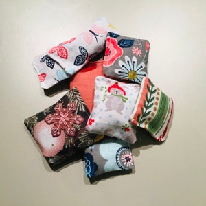 May include: A collection of small, square fabric sachets with various patterns. Designs include butterflies, flowers, a bunny in a hat, a gingerbread cookie, and stripes. The sachets are in shades of white, pink, red, green, gray, and blue.