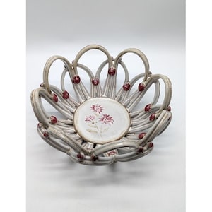 May include: A ceramic basket bowl with a woven lattice design in a light beige finish. The bowl features small, circular red accents at the intersection points of the lattice. The center base displays a painted floral motif in muted red tones.
