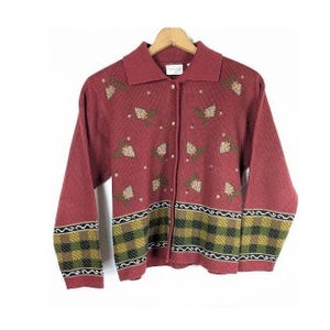 May include: A long-sleeved, button-down knit cardigan in a deep red hue. The garment features a repeating pattern of small, embroidered floral motifs across the chest and a wide, checkered band in shades of green, yellow, and black at the hem.