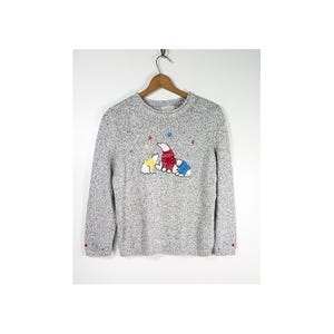 May include: A grey speckled long-sleeve sweater featuring an embroidered graphic of three polar bears wearing sweaters in yellow, red, and blue, surrounded by small colorful star accents. The cuffs also feature small embroidered star details.
