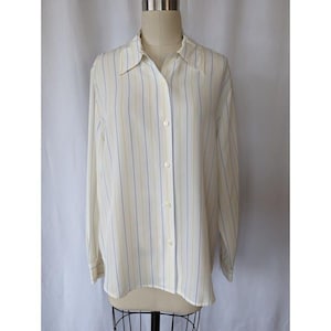 May include: Cream-colored button-down shirt with vertical stripes in light blue and yellow. The long-sleeved shirt is displayed on a mannequin, showcasing its classic collar and button-up front. The fabric appears lightweight.