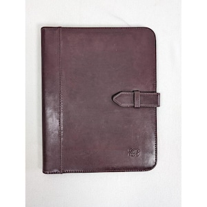 May include: A dark plum-colored leather portfolio case featuring a vertical stitched panel on the left side and a horizontal strap closure on the right. The bottom right corner displays a small, embossed monogram logo with the letters EB.