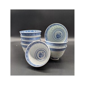 May include: A stack of eight white and blue porcelain bowls. The bowls have a blue floral design in the center and a blue geometric pattern around the rim. The bowls are stacked on a dark surface.