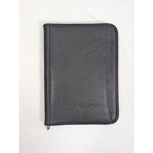 May include: A black zippered portfolio case with a smooth, matte finish. The front cover features a vertical stitched seam detail on the right side and the embossed text Westlaw centered near the bottom edge of the rectangular document holder.