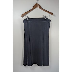 May include: A solid dark gray skirt with a smooth, velvet-like texture. The skirt features a high-waisted design with a straight waistband and a slightly flared, A-line silhouette that falls to a knee-length hem, hanging from a wooden hanger.