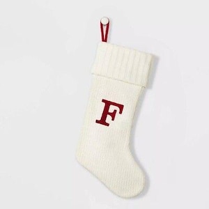 May include: Cream-colored Christmas stocking with a red letter "F" embroidered on the front. The stocking has a ribbed cuff and a red loop for hanging. A festive holiday decoration.