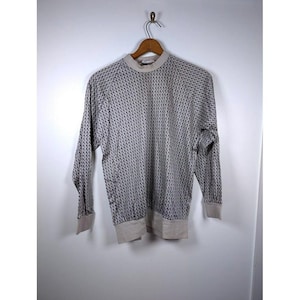 May include: A long-sleeved, light gray sweater with a repeating pattern of small, dark blue dots. The sweater has a crew neck and ribbed cuffs and hem in a lighter gray color. The garment is hanging on a wooden hanger.