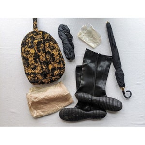 May include: A black and gold patterned bag, a pair of black rain boots, a black umbrella, a clear plastic bag, and a brown paper bag.