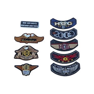 May include: A collection of embroidered patches with various designs and text. The patches feature Harley-Davidson logos, wings, and phrases like "BAD ASS BOY'S" and "LADIES OF HARLEY." Colors include black, gold, red, and blue.