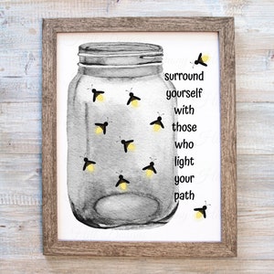 May include: A framed print featuring a watercolor illustration of a mason jar filled with fireflies. The jar is gray, and the fireflies have yellow glowing lights. The text reads, "surround yourself with those who light your path."
