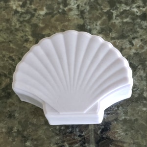 May include: A white ceramic seashell shaped dish. The dish is smooth and has a glossy finish.