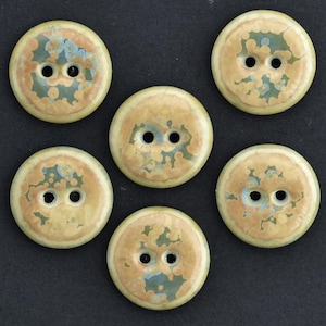 Könnte beinhalten: Sechs runde Knöpfe mit jeweils zwei Löchern. Die Knöpfe haben eine cremefarbene Basis mit einem gesprenkelten Muster aus Beige, Blau und Grün. Die Knöpfe sind auf dunklem Untergrund angeordnet.