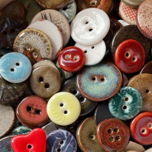 Può includere: Una collezione di bottoni in ceramica di vari colori e dimensioni. I bottoni sono rotondi, con due o quattro fori, e presentano una finitura lucida. I colori includono rosso, bianco, blu, giallo e marrone.