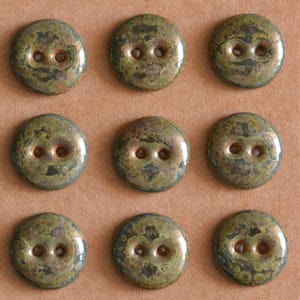 Può includere: Nove bottoni rotondi a due fori con finitura verde e bronzo screziata. I bottoni sono disposti in una griglia di tre per tre, evidenziando il loro aspetto invecchiato e strutturato. Ideali per cucito o progetti artigianali.