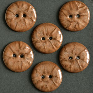 Op de afbeelding: Zes ronde, bruine knopen met elk twee gaten. De knopen hebben een gestructureerd, radiaal ontwerp en een glanzende afwerking. Deze decoratieve knopen zijn geschikt voor naai- en knutselprojecten.