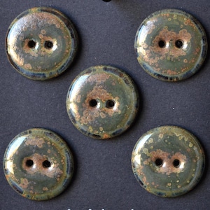 May include: Five ceramic buttons with a glossy finish. The buttons are round, with a dark green base color and speckled brown and gold accents. Each button has two holes for sewing. The buttons are arranged on a dark surface.