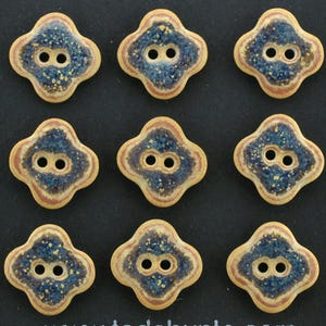 May include: Nine four-lobed ceramic buttons arranged in a grid. Each button features a central dark blue speckled glaze surrounded by concentric bands of light brown and cream. Every button has two circular holes centered in the middle.