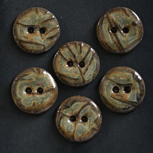May include: Five circular ceramic buttons arranged in a cluster. Each button features a glossy, mottled glaze in shades of sage green, brown, and tan with a distinct two-hole center design and a textured, uneven surface finish throughout the set.