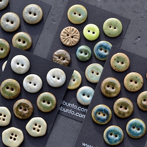 May include: An assortment of ceramic buttons in various colours and patterns, including green, blue, brown, and white. The buttons are arranged on a black surface with the text "www.ubuntu.com" and "www.bunio.com".