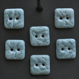 May include: Six square buttons with rounded corners, each featuring a two-hole design and a mottled, light blue-green surface texture with dark, vein-like patterns resembling leaves or organic markings, arranged in a symmetrical layout.