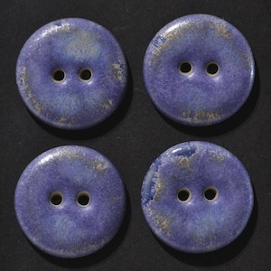 Könnte beinhalten: Ein Set aus vier runden Zweilochknöpfen mit einer glänzenden, gesprenkelten blauen Glasur und subtilen weißen sowie grauen Variationen auf der Oberfläche. Jeder Knopf hat eine glatte, leicht gewölbte Form mit reaktivem Finish.