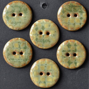 May include: A set of five round ceramic buttons featuring a glossy finish with a mottled green and yellow grid pattern. Each button has two central holes and a smooth, slightly raised surface with subtle brown edges around the perimeter.