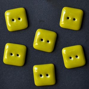 May include: Five square, bright yellow buttons with rounded corners and a smooth, glossy finish. Each button features two centred holes for attachment, arranged horizontally in the middle of the square shape, creating a uniform set of fasteners.