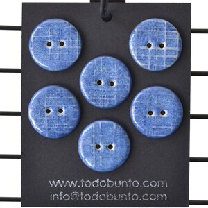May include: Five round blue buttons with a glossy finish and a white grid pattern, each featuring two center holes. The buttons are attached to a black display card printed with the text www.todobunto.com and info@todobunto.com.