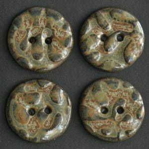 May include: Four round buttons with two holes each. The buttons have a textured surface with a mottled pattern of green, brown, and black. The buttons are likely ceramic or a similar material.