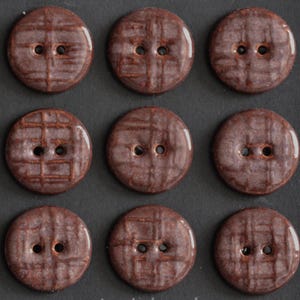 May include: A set of nine circular brown buttons arranged in a three-by-three grid. Each button features a glossy finish, two central holes for attachment, and a subtle, raised grid-like texture across the surface of the brown material.
