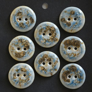 May include: A set of seven round, two-hole buttons featuring a glossy, cream-colored base with mottled patches of blue and brown earth-toned patterns. Each button has a smooth, circular surface with two centered holes for attachment.
