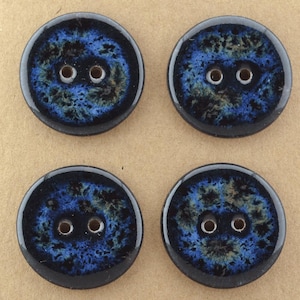 Könnte beinhalten: Ein Set aus vier runden Knöpfen mit zwei Löchern, die eine glänzende Oberfläche mit einem gesprenkelten Muster aus tiefem Blau, Schwarz und braunen Akzenten aufweisen. Jeder Knopf hat einen glatten, erhöhten Rand und eine dunkle, gemusterte Mitte.