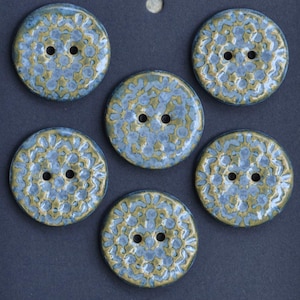 May include: Six round buttons with two holes each. The buttons have a blue and gold floral pattern on a dark background. The buttons are made of a glossy material.
