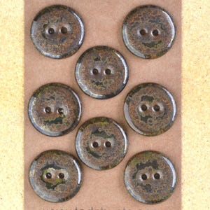 May include: Seven round, two-hole buttons arranged on a brown card. Each button features a mottled, glossy finish with blended shades of dark brown, black, and olive green, creating a textured, earthy appearance across the circular surfaces.