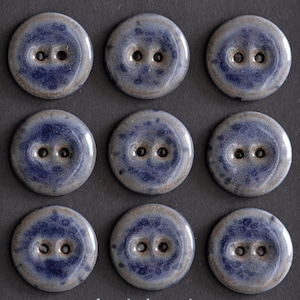 Könnte beinhalten: Neun runde, blau-graue Knöpfe mit jeweils zwei Löchern, angeordnet in einem Raster. Die Knöpfe haben ein gesprenkeltes Design und eine glänzende Oberfläche, geeignet für Näh- oder Bastelprojekte.