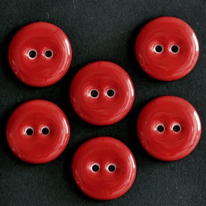 May include: A set of five circular, glossy red buttons, each featuring a smooth, slightly concave center and two small, centered holes for attachment. The buttons are arranged in a cluster, showcasing their uniform bright red color and finish.