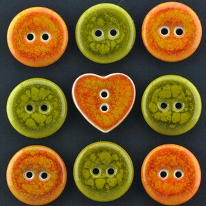 Peut inclure: Un ensemble de neuf boutons disposés en grille, comprenant huit boutons circulaires et un bouton en forme de cœur. Les boutons présentent une finition brillante et marbrée dans des tons orange vif et vert olive, chacun avec deux trous.