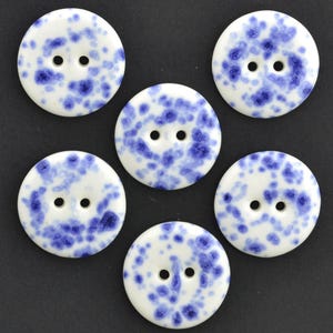 May include: Six round buttons with two holes each. The buttons are white with a blue speckled pattern. The buttons are arranged on a dark background.