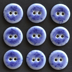 May include: A set of nine round buttons arranged in a three-by-three grid. Each button is light blue with a darker blue mottled or marbled pattern and features two centered holes for attachment. The buttons have a smooth, glossy finish.