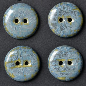 May include: Four round buttons with a marbled design. The buttons are primarily light blue with gold and gray accents. Each button has two holes for sewing.