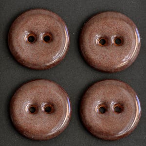 May include: Four round, two-hole buttons with a glossy, speckled brown finish. Each button features a smooth, slightly domed surface with a distinct mottled texture in shades of reddish-brown and tan, arranged in a two-by-two grid pattern.