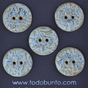 May include: Five ceramic buttons with a cream-colored base and blue and brown decorative patterns. Each button has two holes for sewing. The buttons have a unique, artistic design. The website address www.todobunto.com is visible at the bottom.