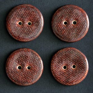 May include: A set of four circular buttons with a glossy, dark reddish-brown finish and a textured, dimpled surface. Each button features two central holes with light-colored edges, arranged horizontally in the middle of the round shape.