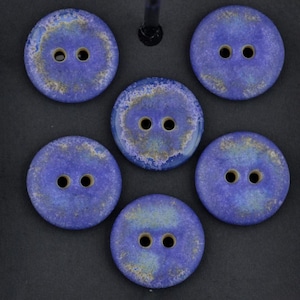Könnte beinhalten: Sechs runde, blaue Knöpfe mit jeweils zwei Löchern. Die Knöpfe haben ein gesprenkeltes Aussehen mit Gold- und Beigetönen, wodurch ein einzigartiger, strukturierter Look entsteht. Diese dekorativen Knöpfe sind ideal für Näh- und Bastelprojekte.