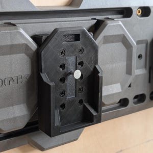 May include: A modular wall-mounted storage system in shades of gray and black. The system features a series of interlocking panels and a black bracket secured with screws. The word "LINK" is embossed on one of the gray panels.